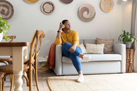 African american woman sitting on gray sofa in cozy living room listening to earbuds