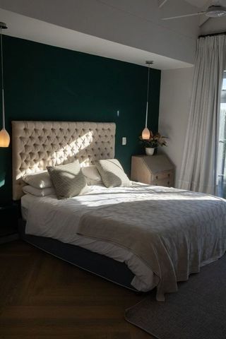 Tufted beige headboard bedroom basking in morning light with deep green accent wall and pendant lamp