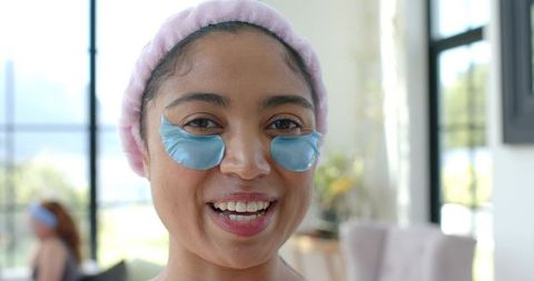 Smiling african american woman wearing blue hydrogel eye patches and pink headband