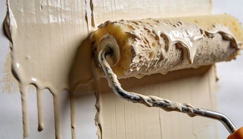Foam roller spreading beige paint with glossy drips and textured wall close-up