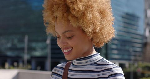 Smiling young woman with curly blonde afro in modern glass city plaza