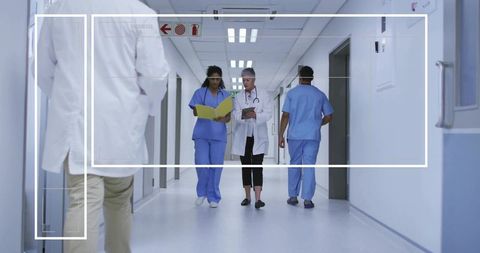 Medical team walking hospital corridor reviewing clinical records and using tablet