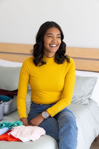 Smiling woman packing suitcase on bed preparing for trip, casual travel lifestyle at home