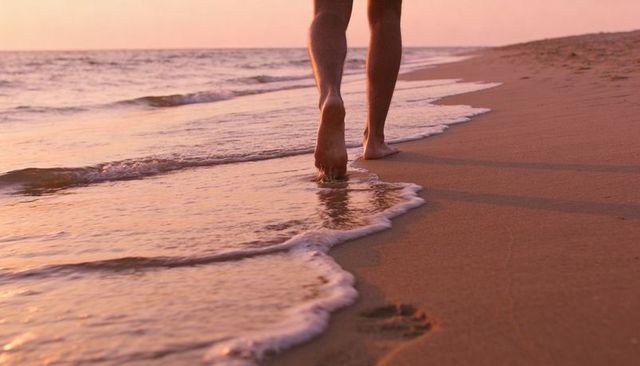 Barefoot walking along sunset shoreline leaving footprints on wet sand with gentle waves