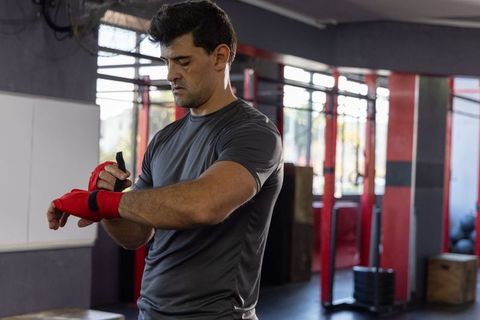 Athlete wrapping red wrist wraps while preparing for boxing and strength training in gym