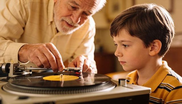 Grandfather teaching grandson how to play vinyl record on turntable sharing nostalgia