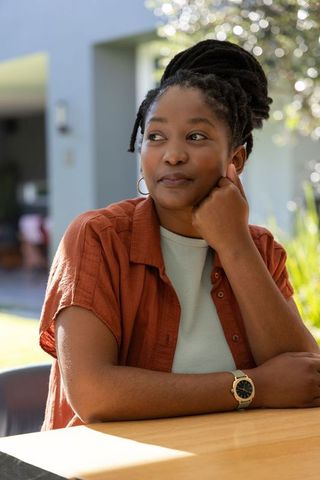 African american woman sitting on patio resting chin wearing rust shirt and watch