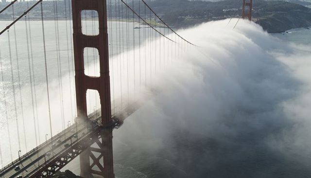 Golden gate bridge tower and cables cutting through rolling fog over san francisco bay