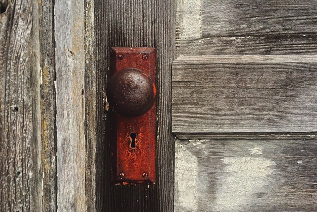 Close-up of a weathered wooden door featuring a rusty doorknob and an antique keyhole. Great for depicting themes of abandonment, vintage, rustic lifestyle, or architectural details. Ideal for use in home improvement blogs, vintage lifestyle storytelling, or textures for web backgrounds.