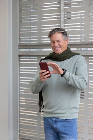 Senior man smiling while using smartphone, wearing scarf and smartwatch outdoor urban