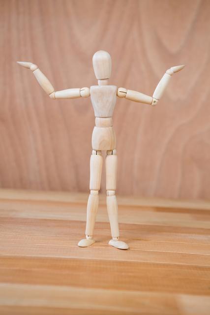 Wooden art mannequin standing with arms outstretched on a wooden floor. Ideal for illustrating concepts of creativity, design, and artistic expression. Useful for art tutorials, design projects, and educational materials.