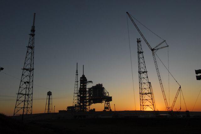 The image showcases a serene dawn at NASA's Kennedy Space Center, highlighting the newly erected lightning towers on Launch Pad 39B. These structures, including a 500-foot-tall tower with a fiberglass mast, are part of the advanced lightning protection system designed for the Constellation Program and Ares/Orion launches. The fixed and rotating service structures of the Space Shuttle Program are also visible. This image is ideal for materials discussing space exploration, advanced engineering projects, or NASA's historic and current programs. Could be useful in educational materials, science and technology publications, or space agency communications.
