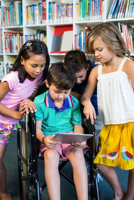 Group of diverse children gathered around a boy in a wheelchair, engaging with a digital tablet in a school library. This image can be used to illustrate themes of inclusive education, technology in learning, and childhood friendship. Ideal for educational materials, school websites, and articles on inclusive practices.