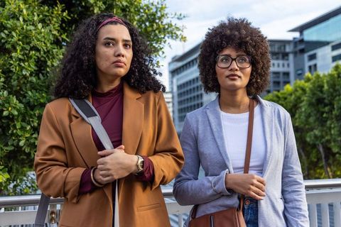 Two professional women standing on city bridge preparing presentation and reviewing data