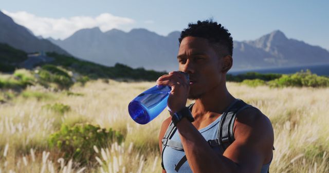 African american man cross country running drinking water in mountain countryside. fitness training and healthy outdoor lifestyle.