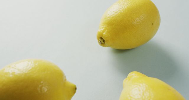 Three vibrant lemons resting on a light background create a vivid contrast that emphasizes their bright yellow color. Perfect for promoting healthy eating, food blogs, cooking websites, and health-oriented content. Use in advertising for lemon-related products, diet plans, and natural ingredients.