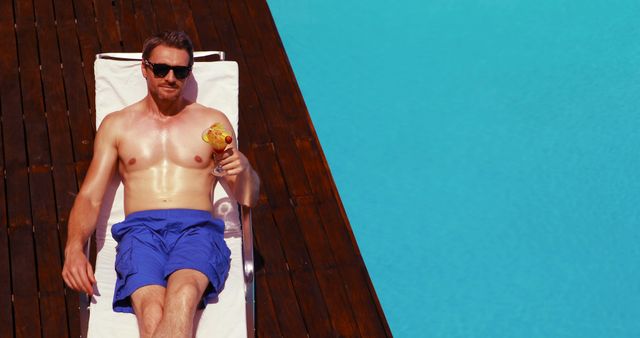 Handsome man holding cocktail on deck chair poolside