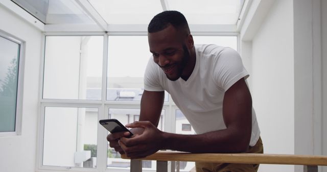 Smiling man enjoying texting on smartphone in modern home - Download Free Stock Images Pikwizard.com