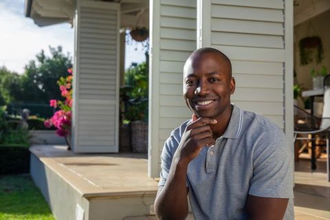 Smiling Man Relaxing on Patio with Blooming Flowers in Sunlit Backyard