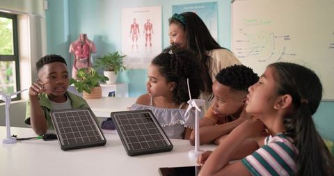 African american teacher guiding kids building solar panels and wind turbines in stem lab