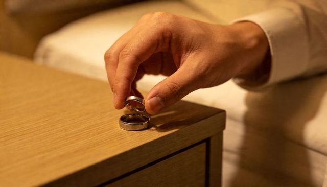 Male hand picking up wedding ring from bedside nightstand in warm lighting