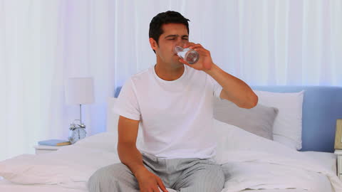 Man Drinking Water and Taking Aspirin on Bed in Morning