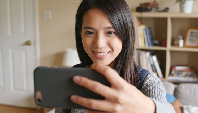 Young asian woman taking selfie with smartphone in living room, wearing gray sweater