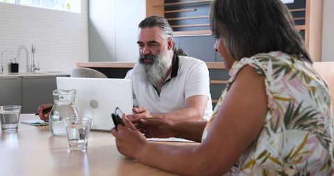 Senior couple planning finances at home with laptop and phone