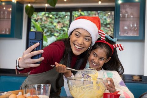 Mom and daughter taking festive selfie while whisking batter and wearing santa hats