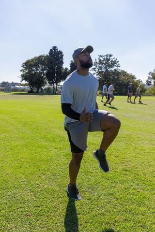African american athlete performing high-knee drill on outdoor grassy field with teammates