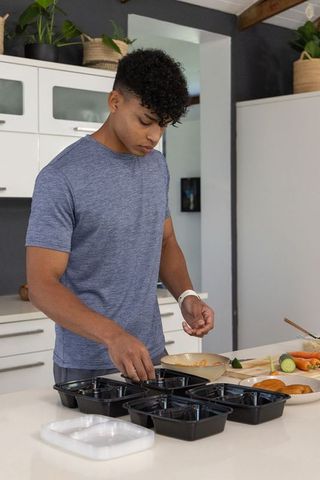 African american man preparing healthy weekly meal prep trays on bright kitchen island