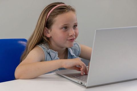 Young girl using laptop at desk learning online and coding with focused expression