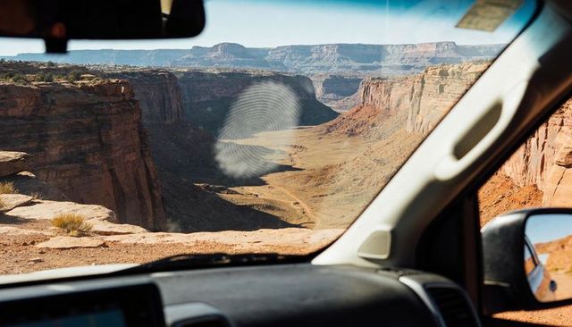 Driving toward desert canyon with windshield fingerprint smudge revealing rugged cliffs