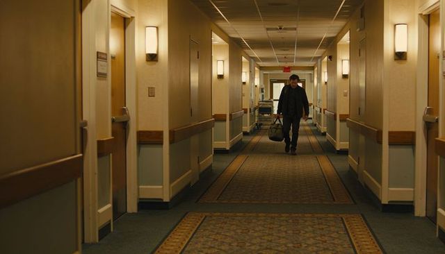 Walking man carrying duffel bag down dimly lit hotel corridor with patterned runner