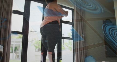 Woman stretching at glass doors preparing for home workout with water bottle and patio