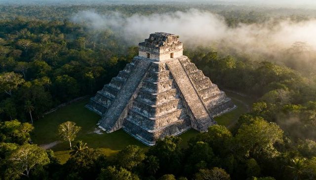 Sunlit maya pyramid rising above misty jungle canopy, ancient stepped temple at dawn
