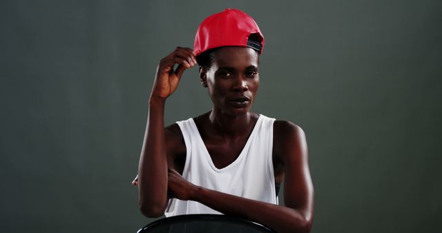 An African American man in a white tank top and red cap poses confidently, with copy space. His relaxed posture and direct gaze convey a sense of cool self-assurance.