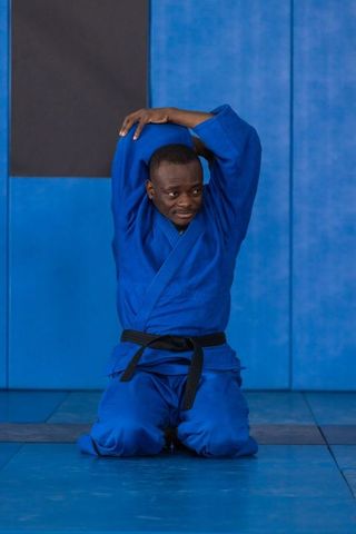 Martial artist kneeling in blue gi on mat in training dojo