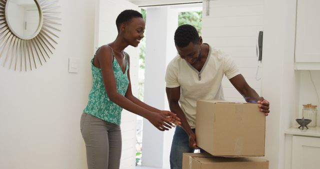 Young couple moving into their new home, actively unpacking several cardboard boxes. They are smiling and seem happy, indicating a harmonious teamwork environment. This can be used for themes related to new beginnings, relocation, family life, domestic settings, and the joys of starting anew in a home.