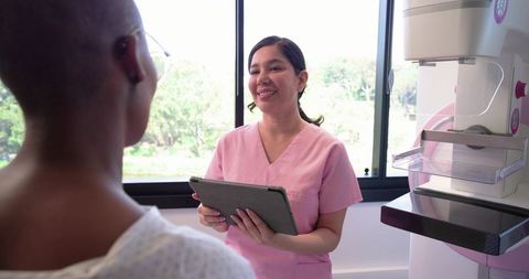 Friendly mammography technologist consulting patient with tablet in screening room