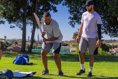 Diverse friends practicing batting with wooden cricket bat in sunny park training session