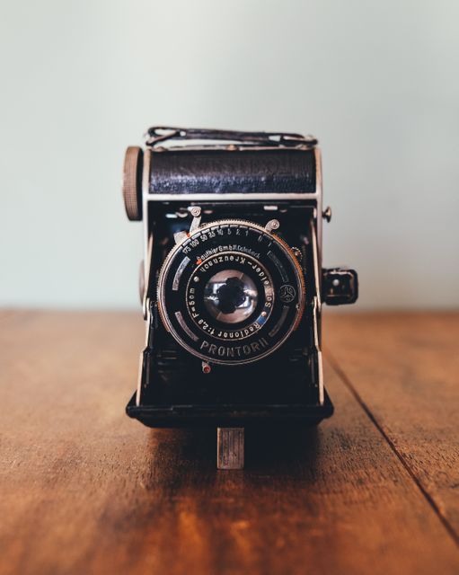 Depicting a vintage film camera placed on a wooden table, this close-up captures the fine details and mechanical beauty of classic photography equipment. Ideal for use in articles or advertisements focusing on the history of photography, retro technology, antique collections, or as a vintage-themed decor element.