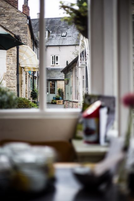 View of quaint village street from inside a cozy café window, natural light illuminating rustic buildings. Ideal for promoting small town tourism, advertisements for cozy cafés or rural eateries, and serene living. Perfect for blogs, travel websites, or lifestyle magazines.