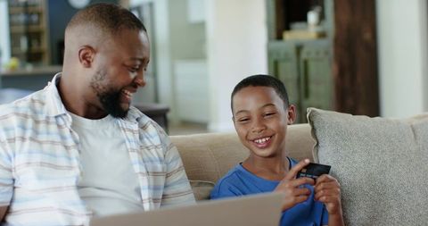 African american father and son sharing online shopping moment on couch with laptop