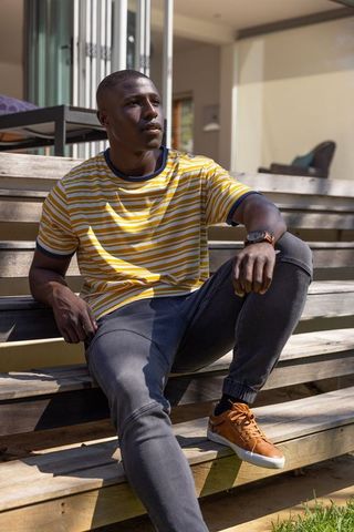 African American man sitting on porch steps wearing striped T-shirt and checking watch