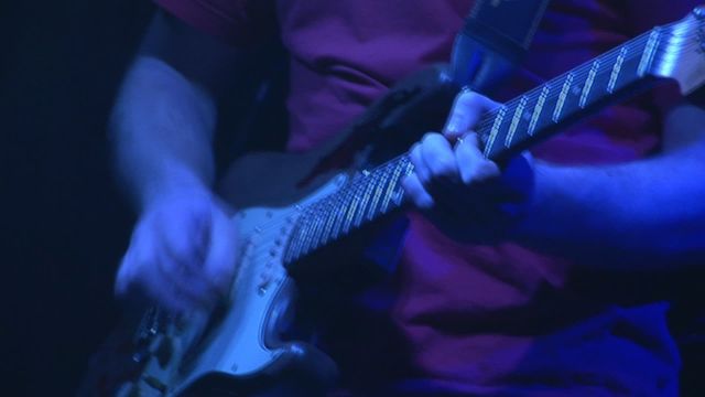 Guitarist performing on stage under blue lighting, highlighting the musician's hands and electric guitar. This video is perfect for use in advertisements and promotions related to music concerts, live performances, rock bands, musical events, or articles about guitarists and music in general.