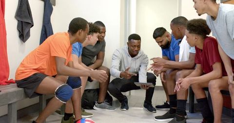 Coach reviewing tactics with diverse male volleyball team in locker room, planning strategy