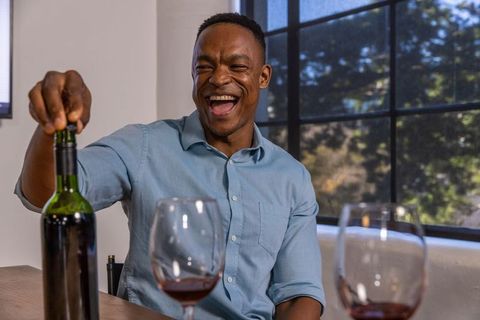 Joyful man opening wine bottle at home gathering