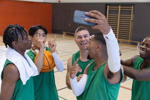 Multiracial basketball teammates celebrating victory taking selfie on indoor court