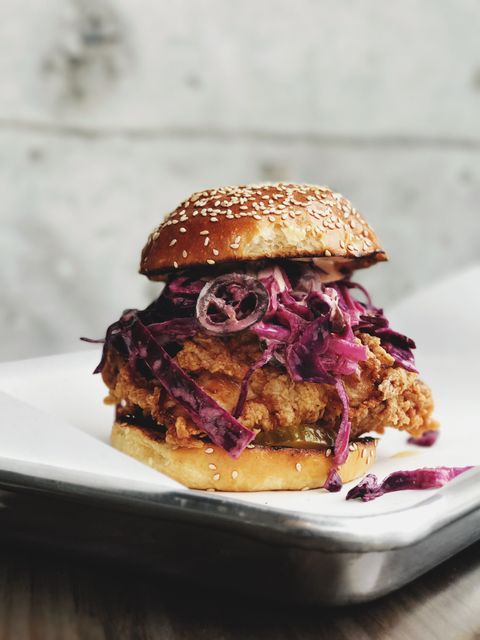 Fried chicken sandwich features sesame bun topped with purple slaw and juicy chicken. Suitable for promoting restaurants, food blogs, menu items, fast food chains, culinary magazines, and takeout advertisements.